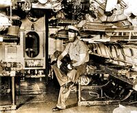 Chief Torpedoman Harold A. Stromsoe sitting in the nearly empty torpedo room of the S-44, 1942. He is holding a M1928A1 Thompson submachine gun, one of several types of small arms carried by USN submarines in WW II.